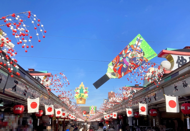 青空の下、日本の提灯や飾りが並ぶ商店街の通り。大きな色鮮やかなバナーが上空に吊るされている。